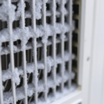 Frozen evaporator coils inside an AC unit with ice crystals and dirt buildup, showing the impact of poor airflow and maintenance.